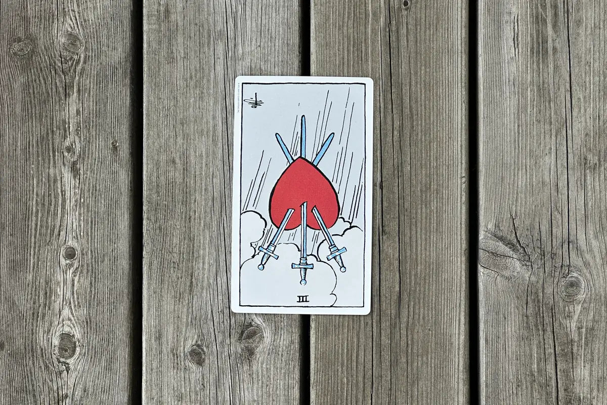 Tre i svärd som omvänt tarotkort mot en träbakgrund