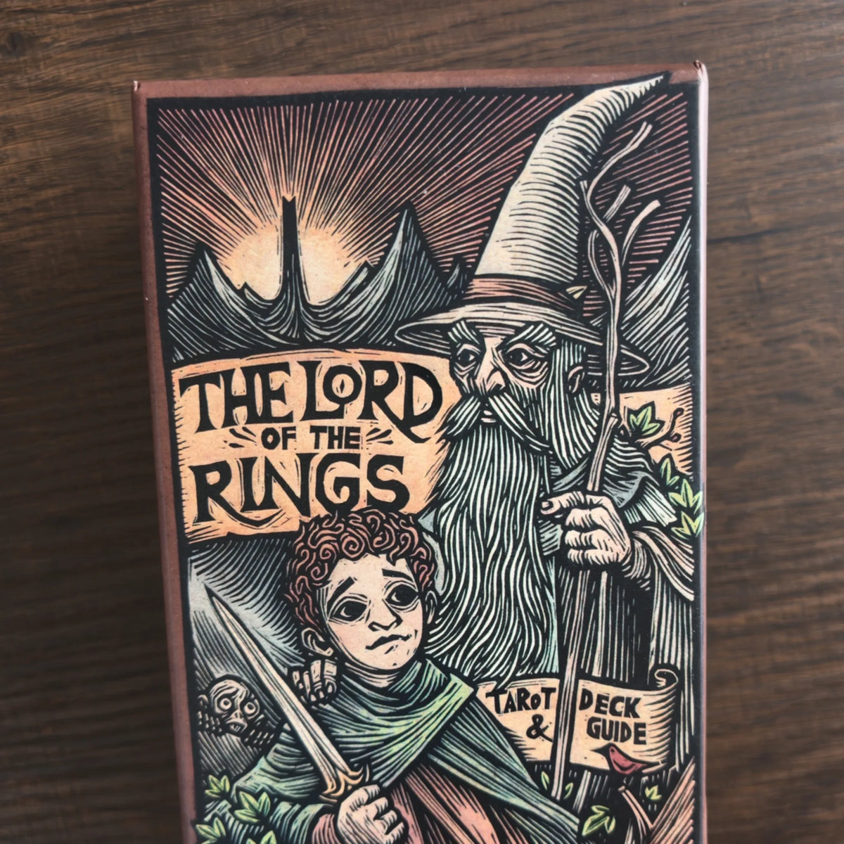 Asken till The Lord of the Rings Tarot Deck & Guide framifrån med träsnittsliknande teckning av en trollkarl och en hobbit