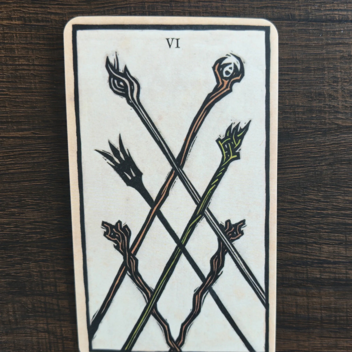 Ett kort märkt VI ur The Lord of the Rings Tarot med sex korsade stavar i svart, orange och grönt på ljus bakgrund