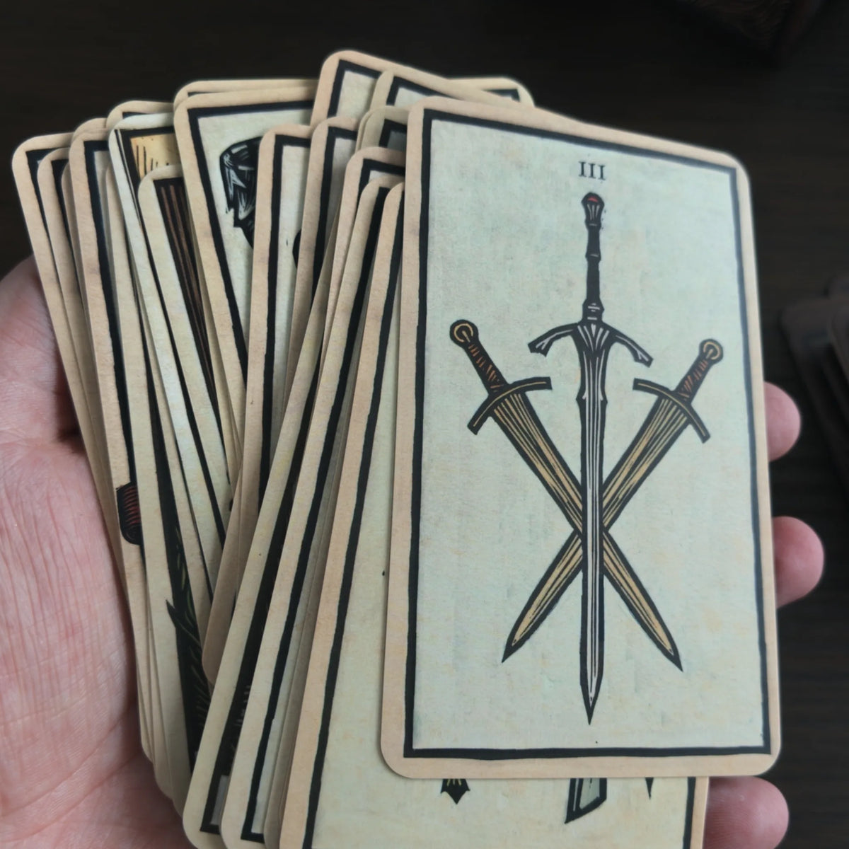 En hand håller en bunt kort ur The Lord of the Rings Tarot, överst ett ljust kort märkt III med tre korsade svärd