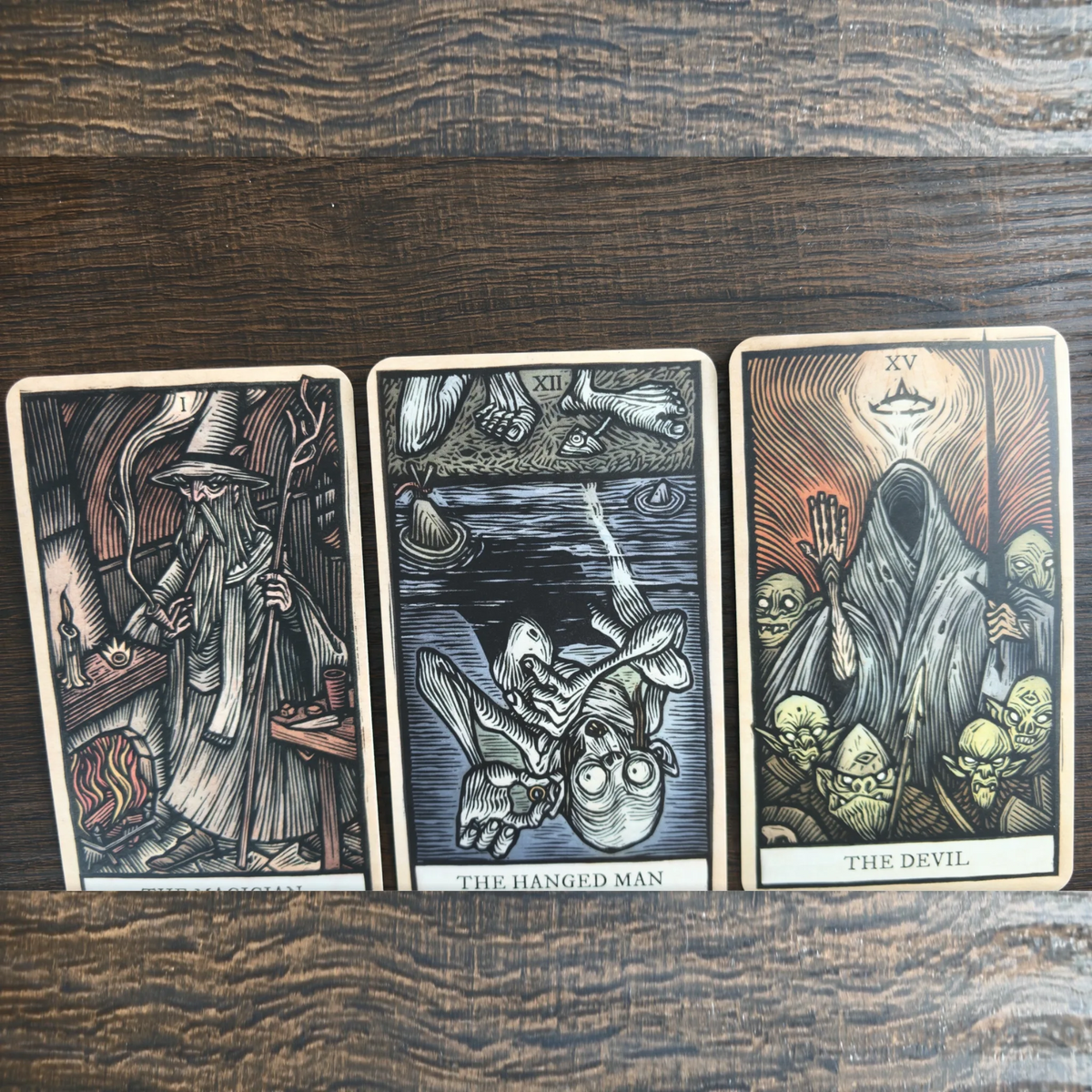 Tre kort ur The Lord of the Rings Tarot bredvid varandra på ett träbord, bland annat The Hanged Man och The Devil
