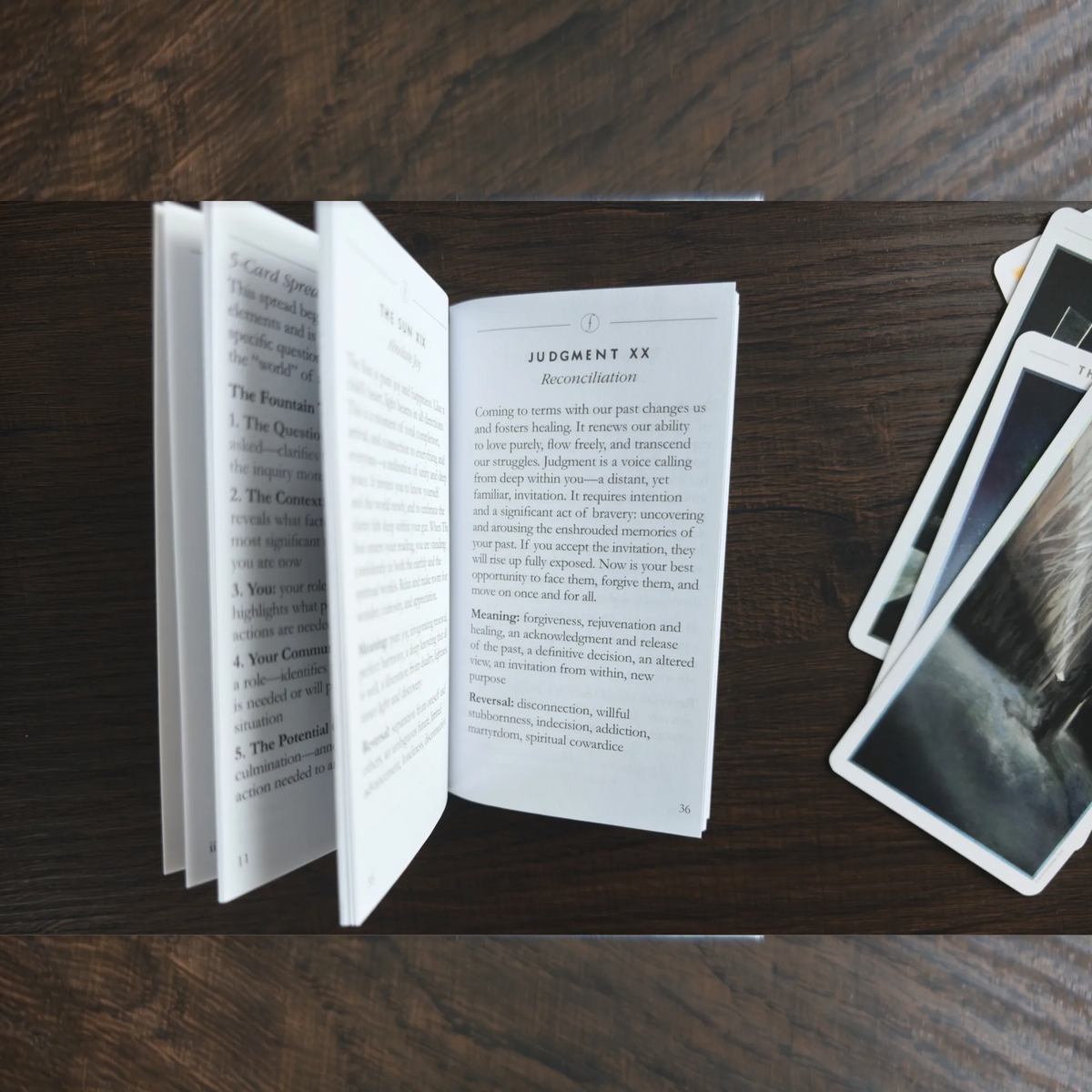 Uppslag i guideboken till The Fountain Tarot med texten om Judgment XX, bredvid några kort på träbordet