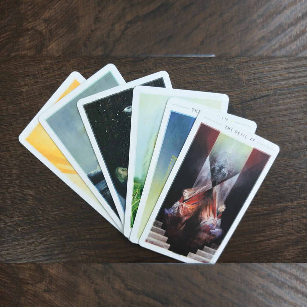 Sex kort ur The Fountain Tarot utlagda som en solfjäder på ett träbord, med The Devil överst