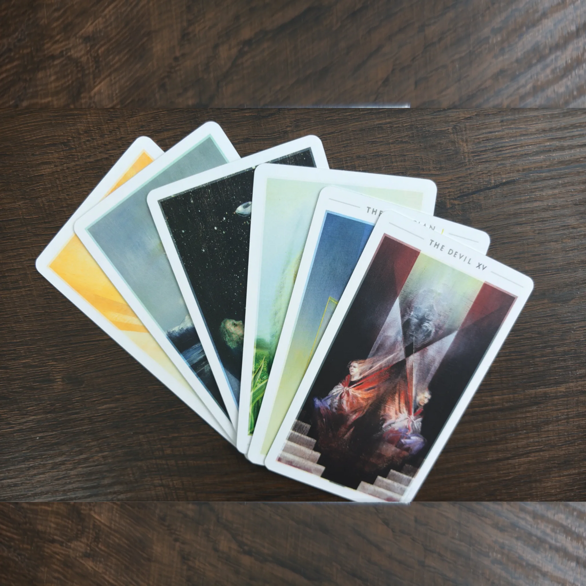Sex kort ur The Fountain Tarot utlagda som en solfjäder på ett träbord, med The Devil överst