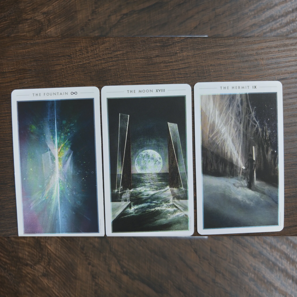 Tre kort ur The Fountain Tarot bredvid varandra på ett träbord: The Fountain, The Moon och The Hermit